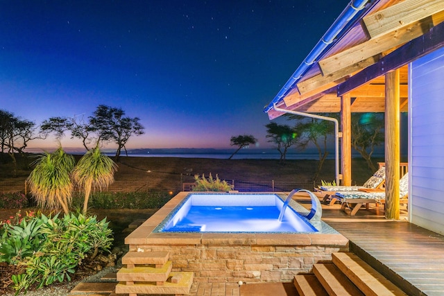 pool at dusk with a water view and an in ground hot tub