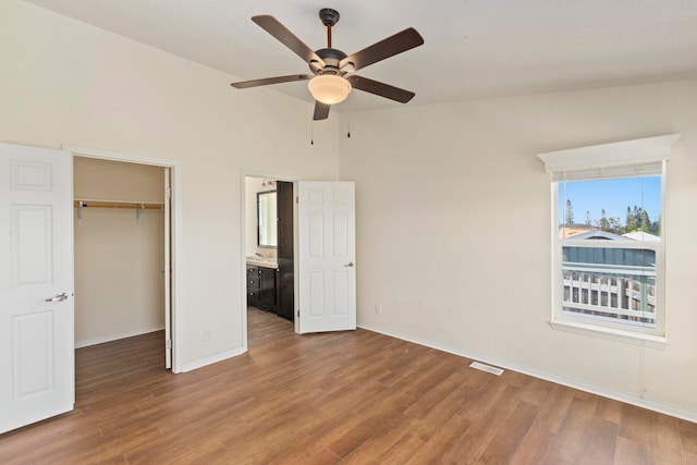 unfurnished bedroom featuring ensuite bath, hardwood / wood-style flooring, ceiling fan, a spacious closet, and a closet