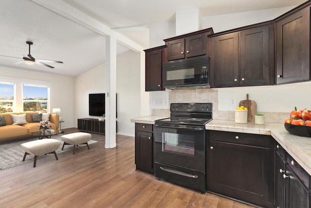 kitchen featuring dark brown cabinetry, ceiling fan, lofted ceiling with beams, light wood finished floors, and black appliances