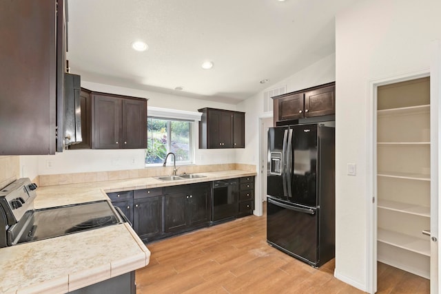 kitchen featuring dark brown cabinetry, sink, light hardwood / wood-style floors, lofted ceiling, and black appliances