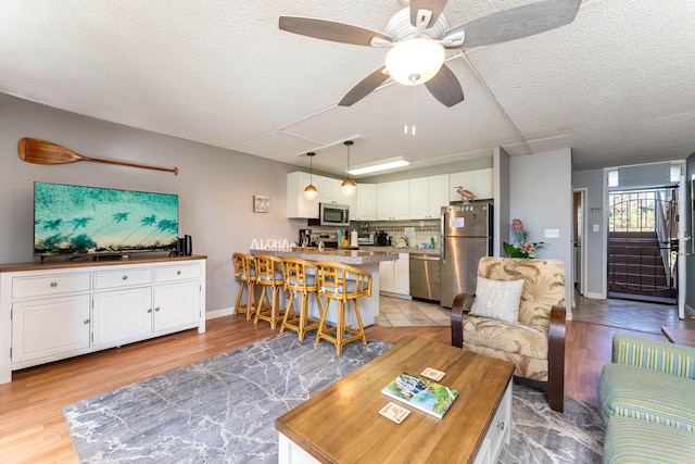 living room featuring ceiling fan, a textured ceiling, and light wood-type flooring