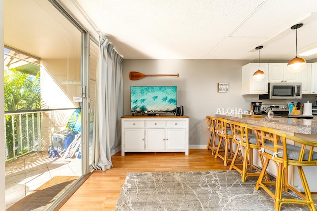 kitchen with stainless steel appliances, white cabinets, light wood-type flooring, and decorative light fixtures