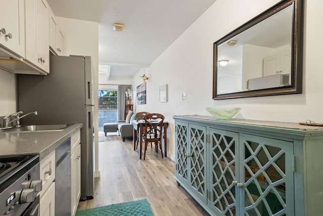 kitchen with sink, white cabinetry, dishwashing machine, light hardwood / wood-style flooring, and stainless steel range