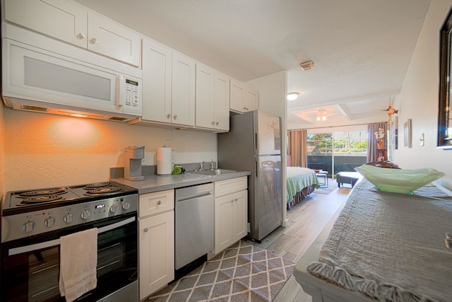 kitchen with appliances with stainless steel finishes, hardwood / wood-style floors, sink, and white cabinetry