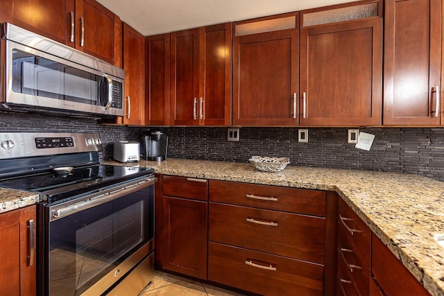 kitchen featuring light tile patterned floors, decorative backsplash, light stone countertops, and stainless steel appliances
