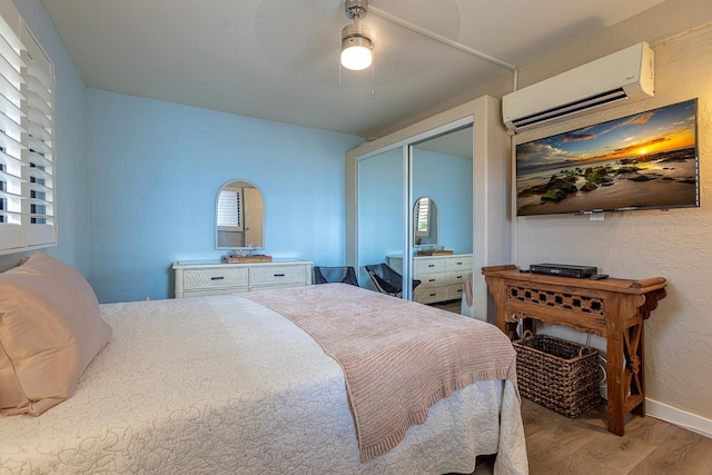 bedroom featuring a ceiling fan, baseboards, wood finished floors, a wall mounted AC, and a closet