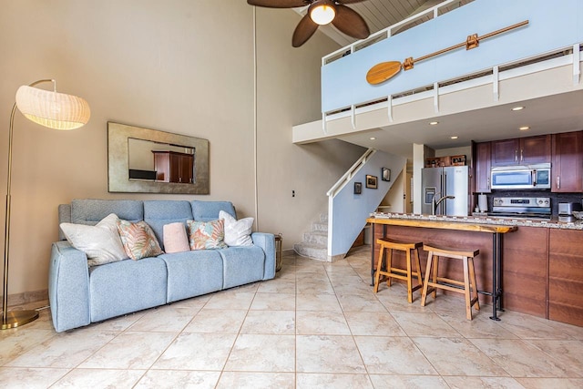 living area with stairs, ceiling fan, and a towering ceiling