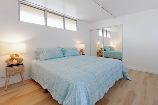 bedroom with a closet, light hardwood / wood-style floors, and track lighting