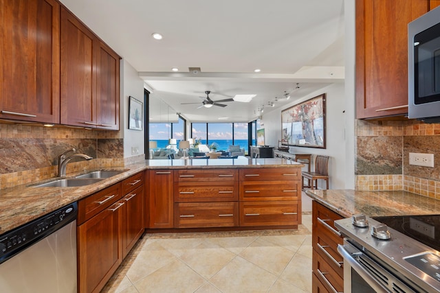 kitchen featuring track lighting, light stone countertops, appliances with stainless steel finishes, backsplash, and a sink