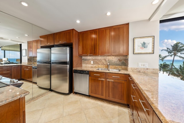 kitchen with appliances with stainless steel finishes, brown cabinets, backsplash, a sink, and light tile patterned flooring