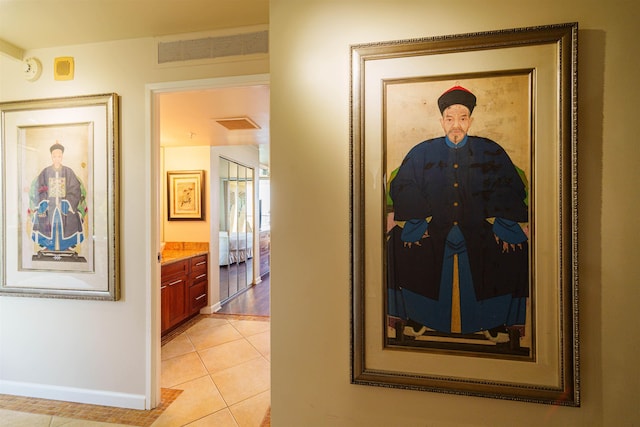 hallway with light tile patterned flooring, visible vents, and baseboards