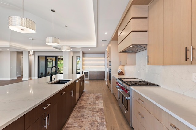 kitchen with light stone counters, sink, hanging light fixtures, and range with two ovens