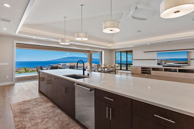 kitchen featuring sink, a raised ceiling, pendant lighting, light hardwood / wood-style floors, and a water view