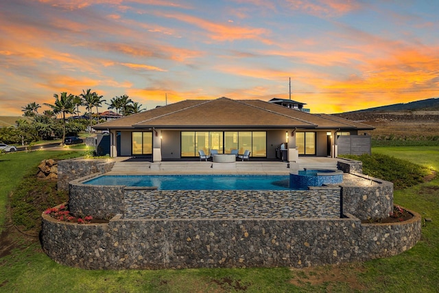 pool at dusk with an in ground hot tub and a patio