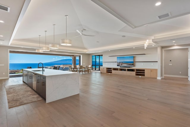 kitchen featuring a large island, sink, a raised ceiling, decorative light fixtures, and a water view