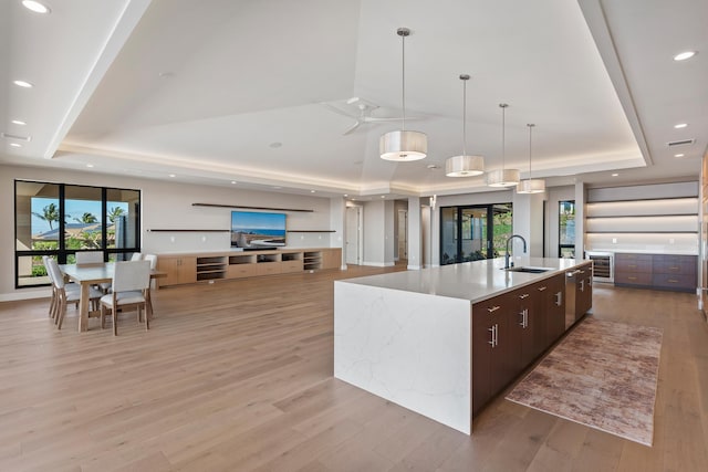 kitchen featuring a large island, dark brown cabinetry, sink, and a tray ceiling