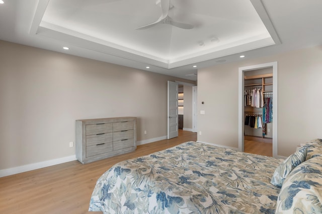 bedroom with a walk in closet, a raised ceiling, ceiling fan, light hardwood / wood-style flooring, and a closet