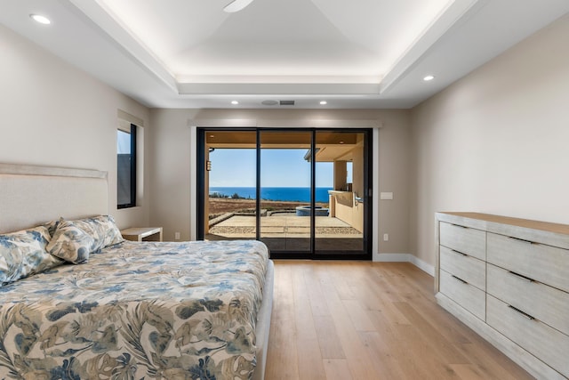 bedroom with access to exterior, a water view, a raised ceiling, and light hardwood / wood-style floors