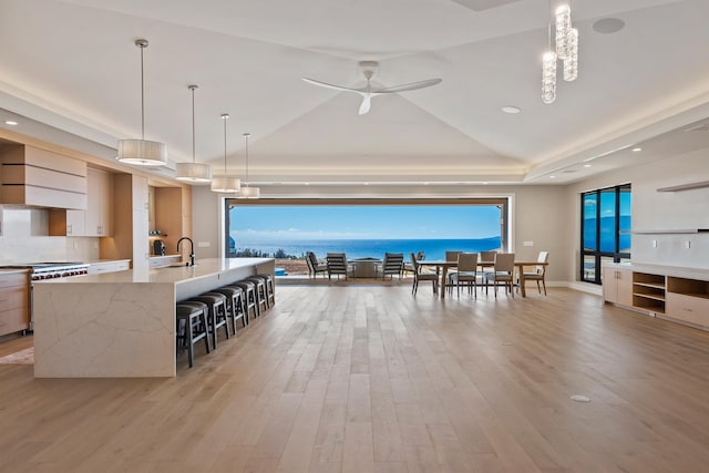 interior space featuring a spacious island, a raised ceiling, a water view, hanging light fixtures, and light stone countertops