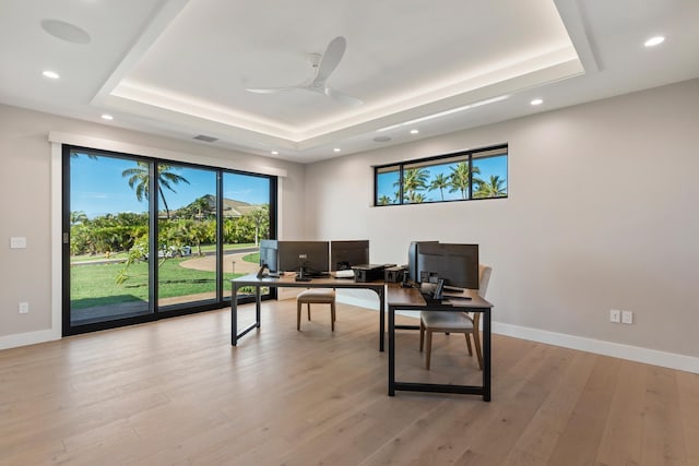 office featuring ceiling fan, light wood-type flooring, and a tray ceiling