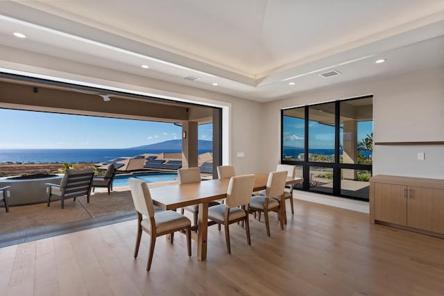 dining room with a tray ceiling, light hardwood / wood-style flooring, and a water view