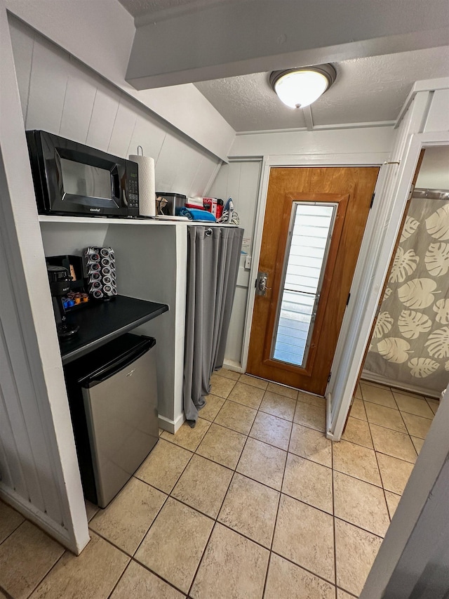 kitchen with light tile patterned flooring, stainless steel fridge, dishwashing machine, and a textured ceiling