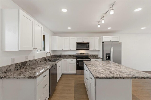 kitchen featuring a center island, sink, light stone counters, white cabinetry, and stainless steel appliances