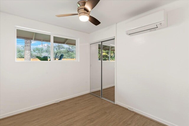 unfurnished bedroom featuring a wall unit AC, ceiling fan, a closet, and hardwood / wood-style floors