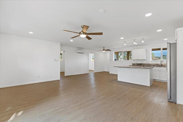 unfurnished living room with light wood-type flooring, a wall unit AC, ceiling fan, and sink