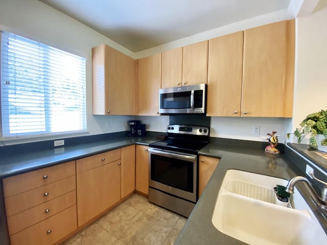 kitchen with light tile patterned flooring, appliances with stainless steel finishes, light brown cabinetry, and sink