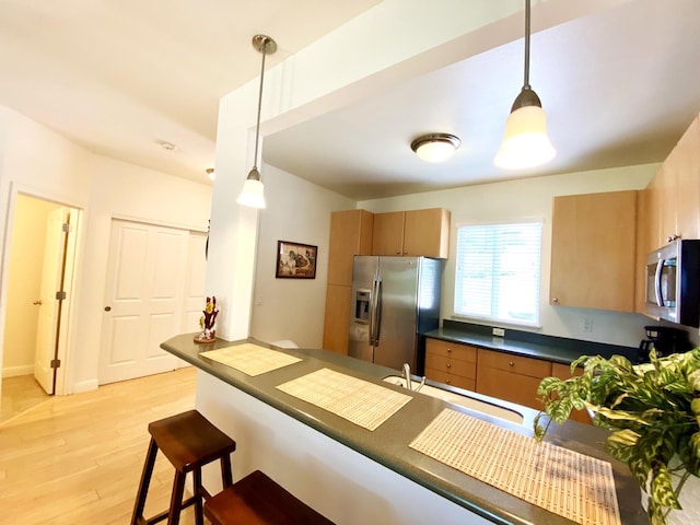 kitchen with appliances with stainless steel finishes, light hardwood / wood-style flooring, kitchen peninsula, and decorative light fixtures