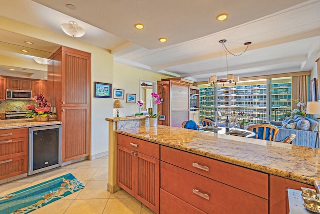 kitchen with tasteful backsplash, light stone countertops, light tile patterned floors, pendant lighting, and beverage cooler