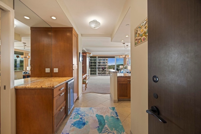 kitchen featuring light stone counters, light tile patterned floors, kitchen peninsula, beverage cooler, and a notable chandelier