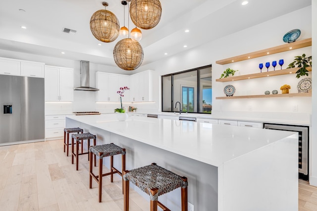 kitchen with wall chimney exhaust hood, decorative light fixtures, white cabinetry, stainless steel fridge with ice dispenser, and a kitchen island