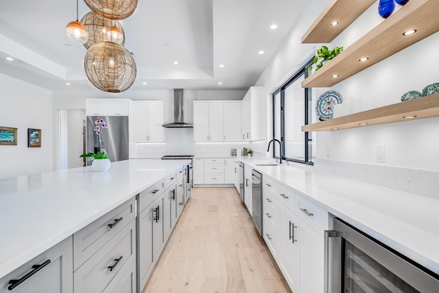 kitchen with sink, wall chimney exhaust hood, decorative light fixtures, white cabinetry, and stainless steel appliances