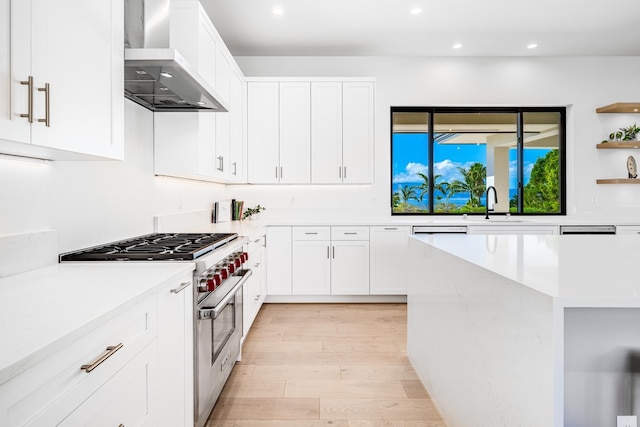 kitchen with sink, wall chimney range hood, high end range, light hardwood / wood-style flooring, and white cabinets