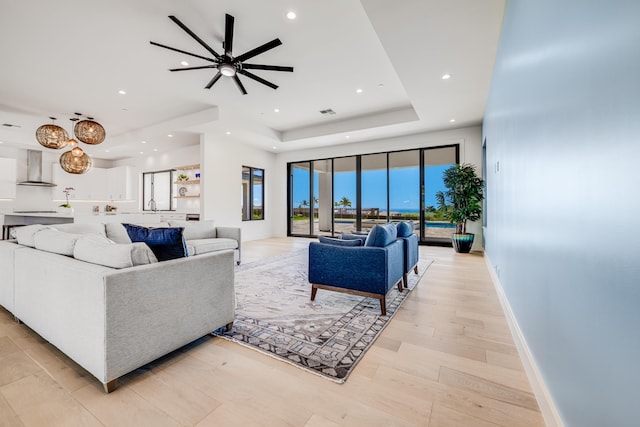 living room featuring ceiling fan, light hardwood / wood-style floors, and a raised ceiling