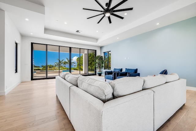 living room featuring a tray ceiling, ceiling fan, and light hardwood / wood-style flooring