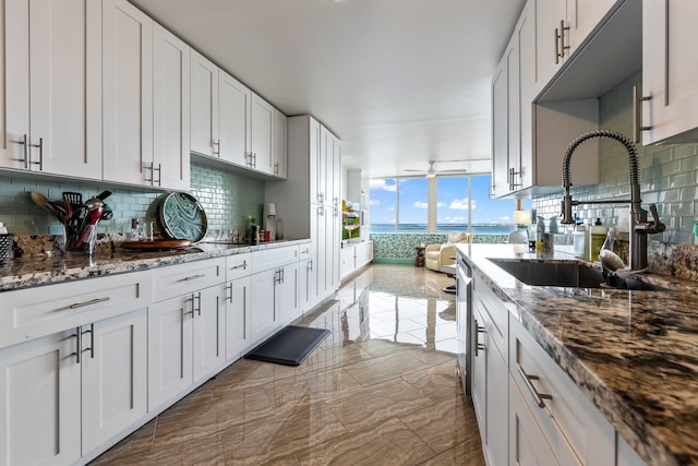 kitchen featuring a sink, tasteful backsplash, white cabinetry, stone countertops, and floor to ceiling windows