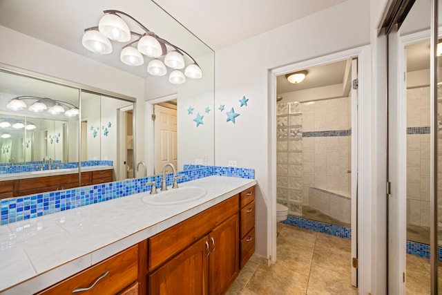 bathroom with toilet, tile patterned flooring, vanity, and tiled shower