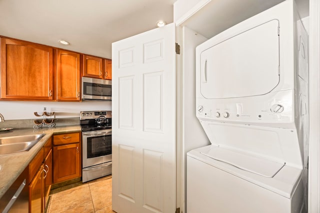 kitchen with light tile patterned flooring, appliances with stainless steel finishes, stacked washing maching and dryer, and sink