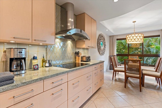 kitchen with light stone countertops, light brown cabinets, wall chimney range hood, hanging light fixtures, and black electric stovetop