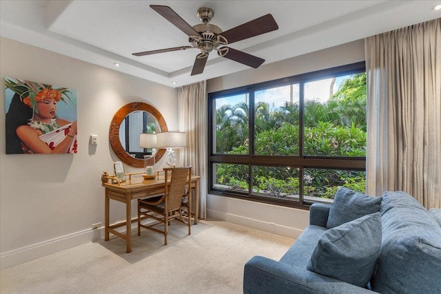 carpeted home office with ceiling fan and a tray ceiling