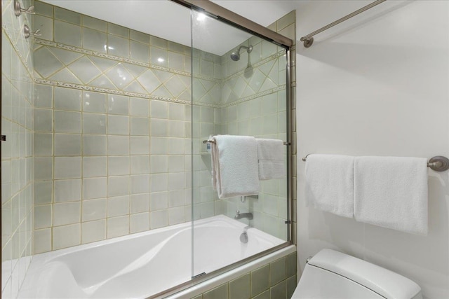 bathroom featuring toilet and shower / bath combination with glass door