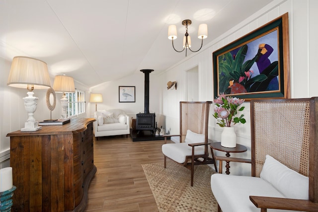 sitting room featuring a wood stove, hardwood / wood-style floors, vaulted ceiling, and an inviting chandelier