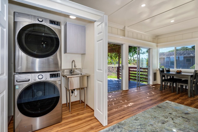 clothes washing area featuring sink, light hardwood / wood-style flooring, and stacked washing maching and dryer