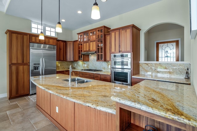 kitchen with pendant lighting, stainless steel appliances, sink, and light stone counters