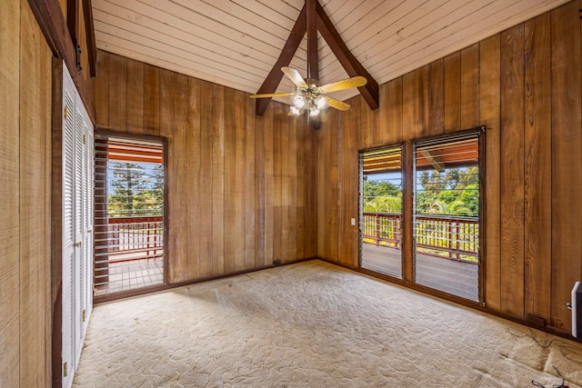 carpeted spare room featuring beamed ceiling, high vaulted ceiling, ceiling fan, and wooden walls