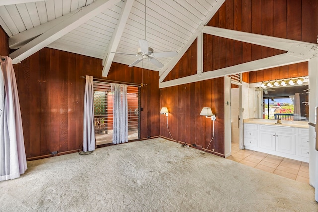 unfurnished living room featuring wood walls, light carpet, high vaulted ceiling, ceiling fan, and beamed ceiling