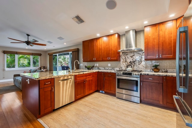 kitchen with sink, appliances with stainless steel finishes, tasteful backsplash, wall chimney exhaust hood, and light hardwood / wood-style flooring